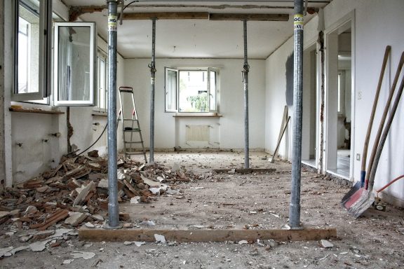 Leeres Zimmer mit Baustellenstützen und aufgeräumtem Schutt am Boden.