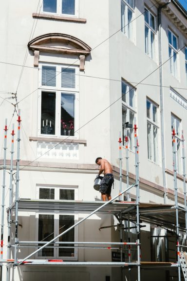 Arbeiter auf einem Gerüst, der an einer Hausfassade arbeitet.