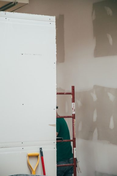 Handwerker steht auf einer Leiter, während er eine Wand bearbeitet.