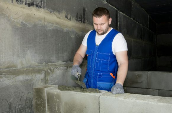 Ein Arbeiter mauert mit einer Kelle in einem Baustellenbereich.